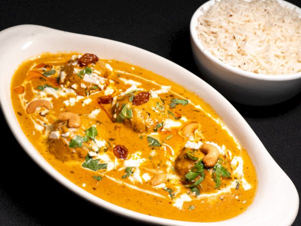 The image shows a dish of creamy curry garnished with herbs and nuts, served alongside a bowl of white rice.