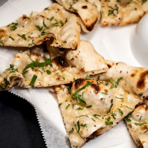 Sliced naan bread topped with herbs, arranged on a white plate and parchment paper.