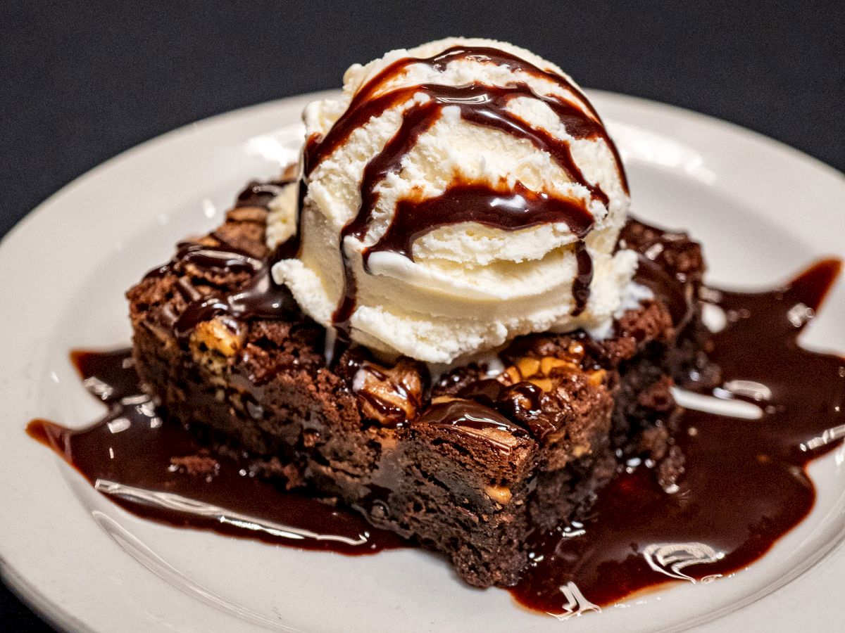 A decadent brownie topped with whipped cream, drizzled chocolate sauce, and a splash of berry sauce on a white plate.
