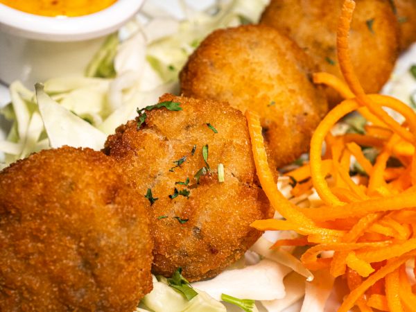 Fried croquettes on shredded cabbage with a swirl of carrots, served with a side of orange dipping sauce on a white plate.