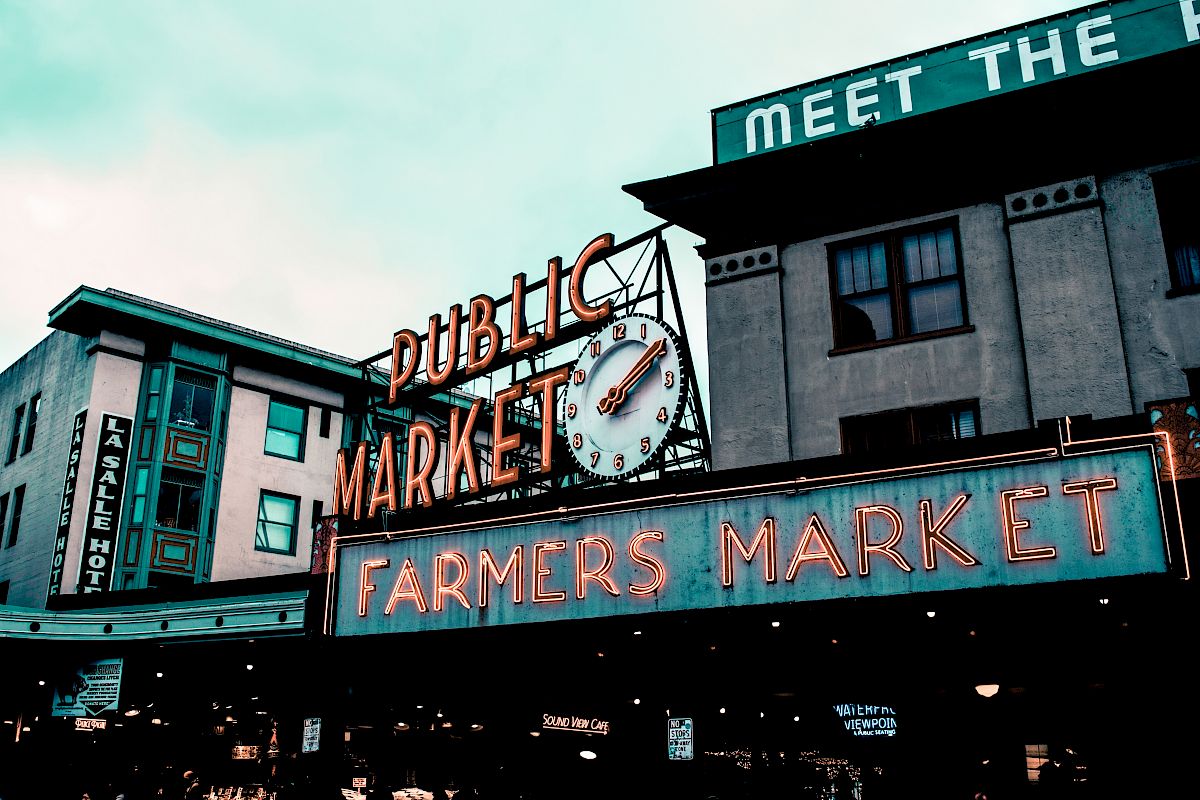 The image shows a public market with signs reading "Public Market" and "Farmers Market," featuring a clock and urban buildings in the background.