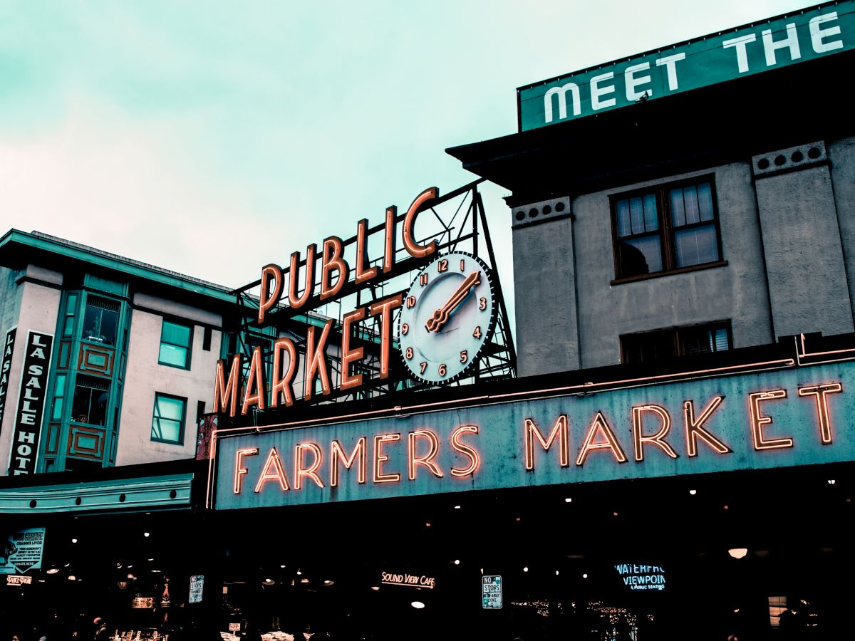 The image shows a public market with signs reading "Public Market" and "Farmers Market," featuring a clock and urban buildings in the background.