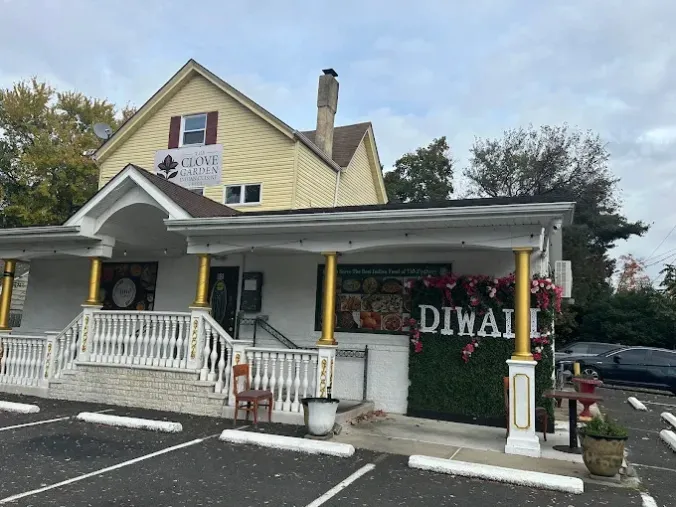 A small roadside storefront with a Diwali decorations backdrop, flowers, and a parked car beside the building.