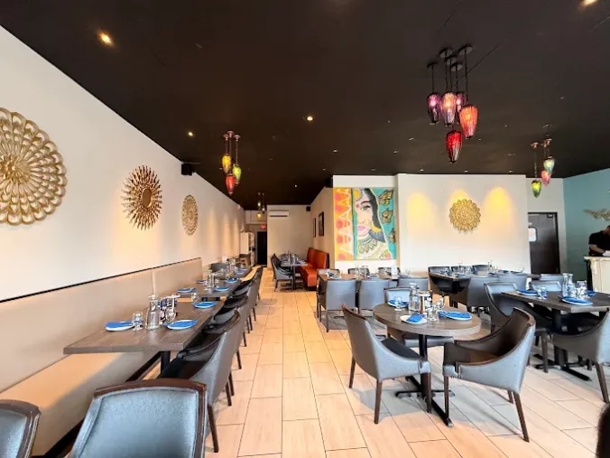A modern restaurant dining room with neatly set tables, gray chairs, pendant lights, and decorative gold wall art.