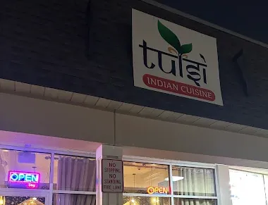 An Indian cuisine restaurant storefront with &ldquo;Taj&rdquo; sign and glowing &ldquo;OPEN&rdquo; lights in the windows, outside at night.